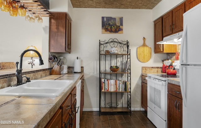 kitchen with under cabinet range hood, white appliances, dark wood-style flooring, a sink, and brown cabinetry