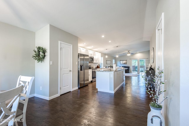 kitchen with pendant lighting, lofted ceiling, a kitchen island, white cabinetry, and stainless steel appliances