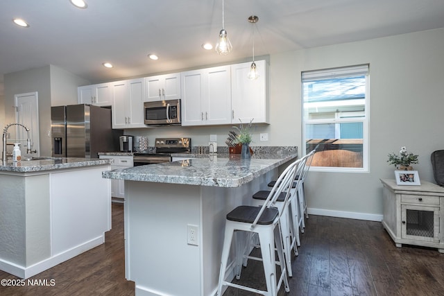 kitchen featuring kitchen peninsula, pendant lighting, white cabinets, a breakfast bar, and stainless steel appliances