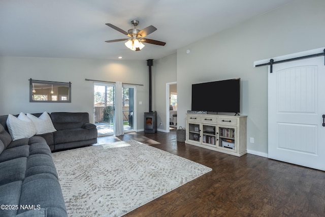 living room with ceiling fan, dark wood-type flooring, a wood stove, a barn door, and lofted ceiling