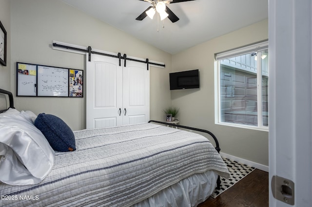 bedroom with vaulted ceiling, ceiling fan, dark hardwood / wood-style flooring, a barn door, and a closet