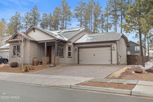 view of front of house with an attached garage, decorative driveway, fence, and solar panels