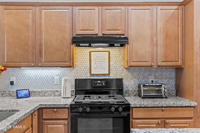 kitchen with light stone counters, a toaster, under cabinet range hood, black gas stove, and decorative backsplash