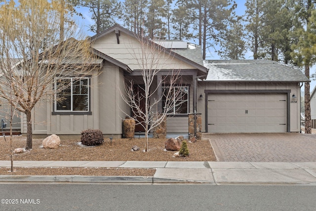 view of front facade with a garage, a shingled roof, and decorative driveway