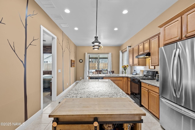 kitchen featuring light tile patterned floors, under cabinet range hood, a sink, black range with gas stovetop, and freestanding refrigerator