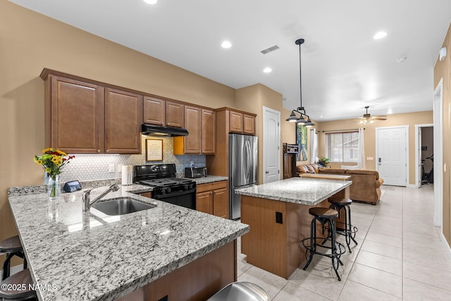 kitchen featuring visible vents, freestanding refrigerator, black gas stove, a sink, and a kitchen breakfast bar