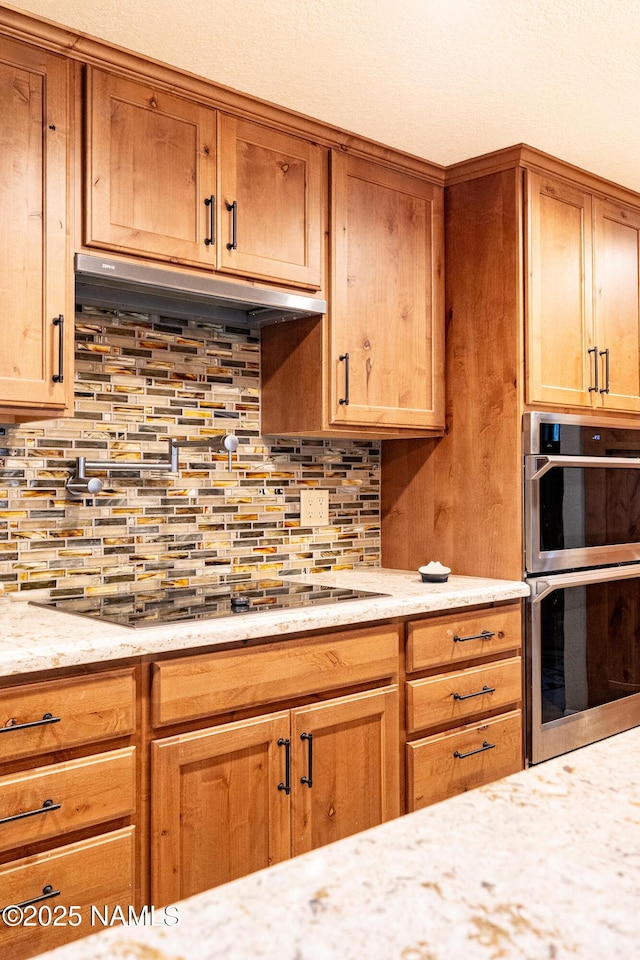 kitchen with tasteful backsplash, light stone countertops, stainless steel double oven, and black electric cooktop
