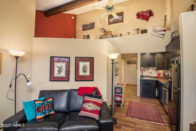 living area with beamed ceiling, wood finished floors, a ceiling fan, and a towering ceiling