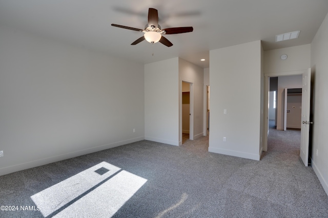 unfurnished bedroom with light carpet, a spacious closet, and ceiling fan