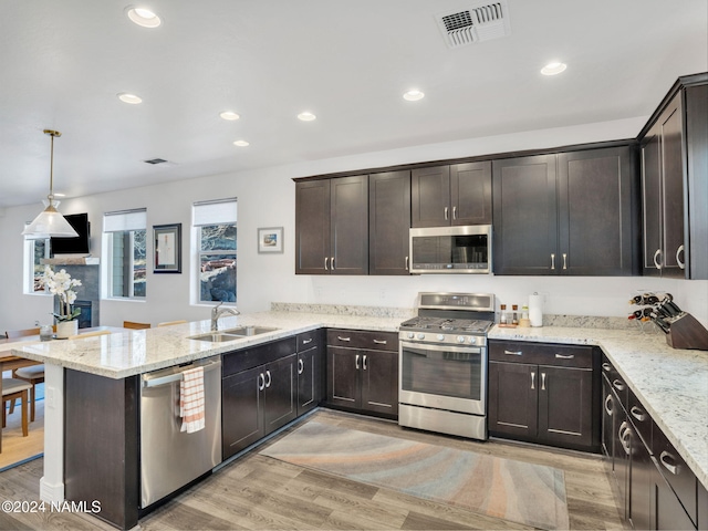 kitchen with appliances with stainless steel finishes, hanging light fixtures, sink, light hardwood / wood-style flooring, and kitchen peninsula