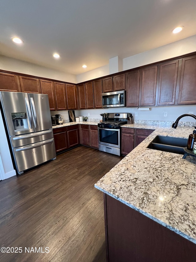 kitchen with dark wood-type flooring, sink, dark brown cabinets, appliances with stainless steel finishes, and light stone countertops