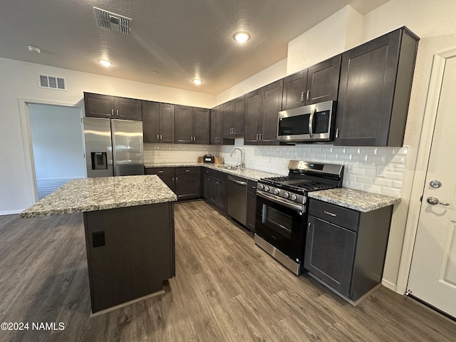 kitchen with a center island, light stone countertops, wood-type flooring, sink, and stainless steel appliances