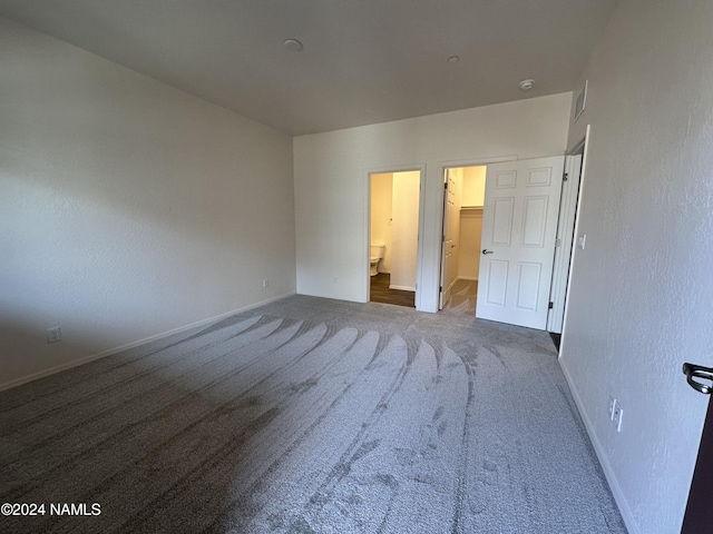 unfurnished bedroom featuring carpet floors, a spacious closet, and ensuite bathroom