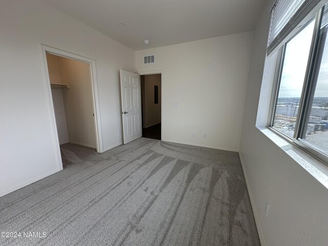 unfurnished bedroom featuring a spacious closet, a closet, and light carpet