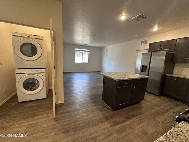 kitchen with dark wood-type flooring, stainless steel fridge with ice dispenser, stacked washing maching and dryer, and a kitchen island