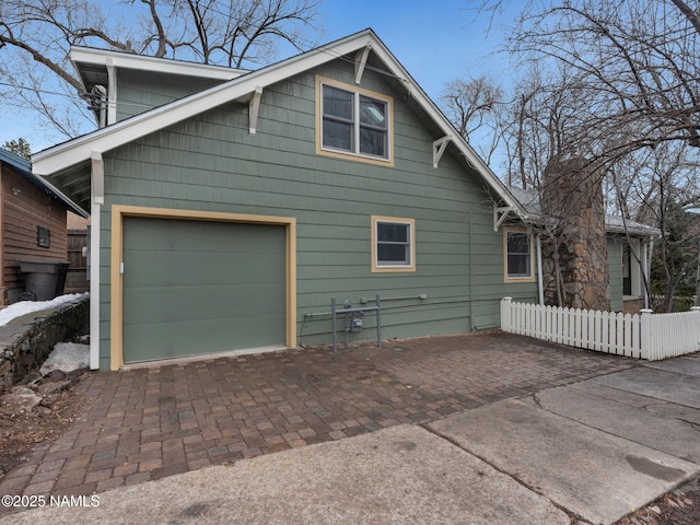 view of property exterior featuring a garage, decorative driveway, and fence