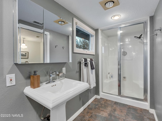 full bath featuring visible vents, baseboards, a sink, a shower stall, and a textured ceiling