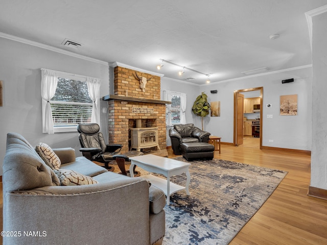 living room with baseboards, visible vents, a wood stove, ornamental molding, and light wood-style floors