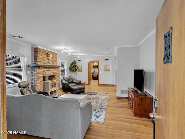 living area featuring light wood-type flooring, visible vents, crown molding, baseboards, and a brick fireplace