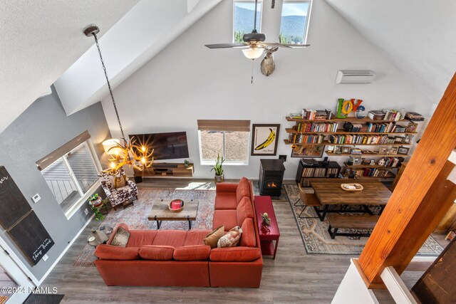 living room with hardwood / wood-style floors, a wood stove, a high ceiling, ceiling fan with notable chandelier, and a wall mounted AC