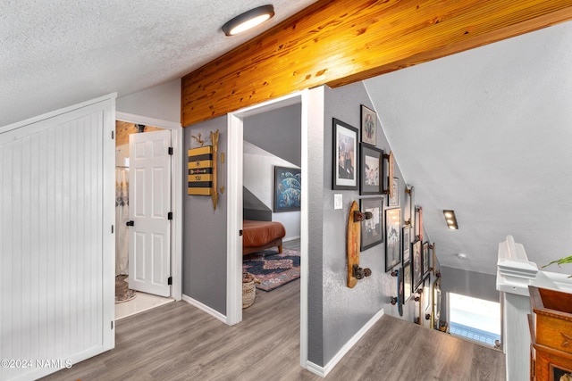 hallway with hardwood / wood-style flooring, a textured ceiling, and vaulted ceiling