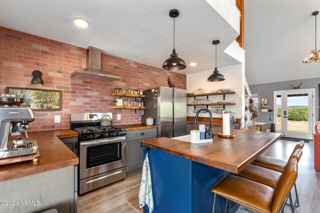 kitchen with appliances with stainless steel finishes, wooden counters, a kitchen breakfast bar, wall chimney range hood, and light hardwood / wood-style flooring