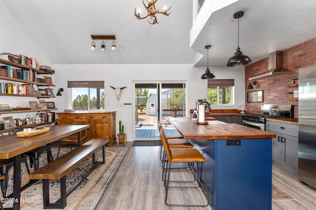 kitchen featuring light hardwood / wood-style flooring, wall chimney exhaust hood, decorative light fixtures, butcher block countertops, and stainless steel appliances