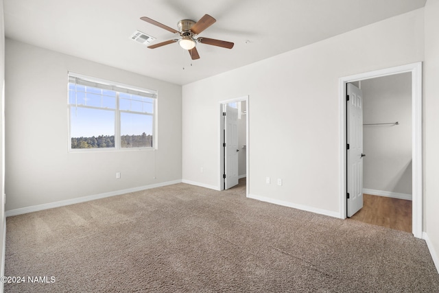 unfurnished bedroom featuring light carpet, a closet, ceiling fan, and a walk in closet