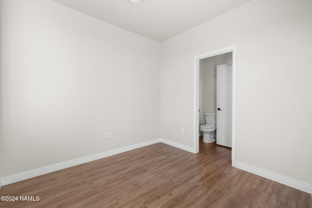 unfurnished bedroom featuring ensuite bathroom and hardwood / wood-style floors