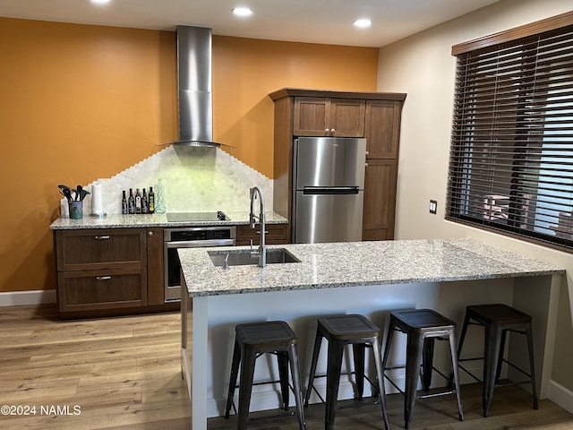 kitchen featuring wall chimney exhaust hood, sink, light stone countertops, a breakfast bar, and stainless steel appliances