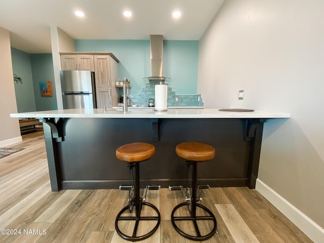 kitchen with light wood-type flooring, exhaust hood, a breakfast bar area, and stainless steel refrigerator