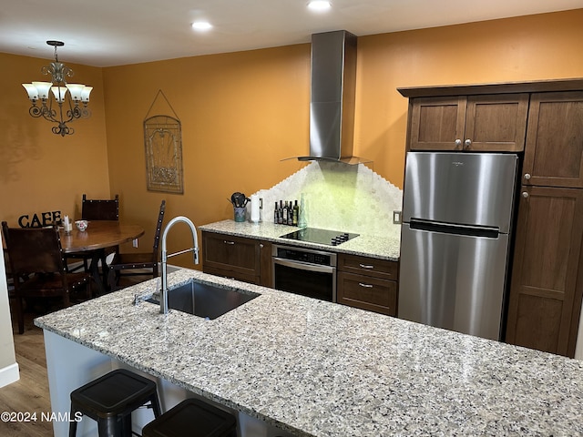 kitchen with wood-type flooring, sink, wall chimney exhaust hood, light stone counters, and stainless steel appliances