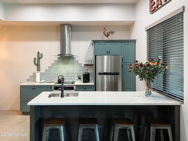 kitchen with wall chimney exhaust hood, a kitchen bar, tasteful backsplash, sink, and stainless steel refrigerator