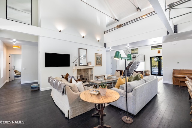 living area featuring dark wood-style floors, a fireplace, baseboards, a towering ceiling, and stairs