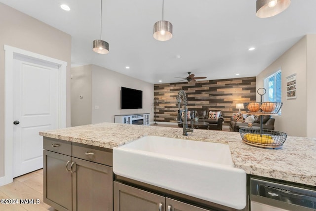 kitchen featuring pendant lighting, wooden walls, sink, ceiling fan, and stainless steel dishwasher