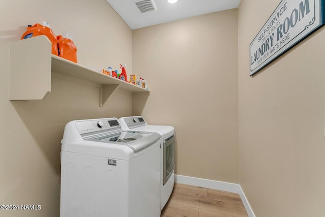 clothes washing area with independent washer and dryer and light wood-type flooring