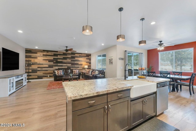 kitchen featuring dishwasher, hanging light fixtures, sink, light stone counters, and wood walls