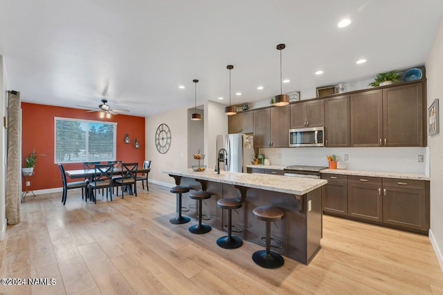 kitchen featuring pendant lighting, light stone counters, a breakfast bar, a center island with sink, and stainless steel appliances