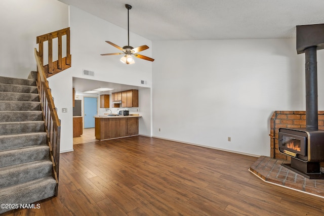 unfurnished living room with visible vents, ceiling fan, dark wood finished floors, stairway, and a wood stove