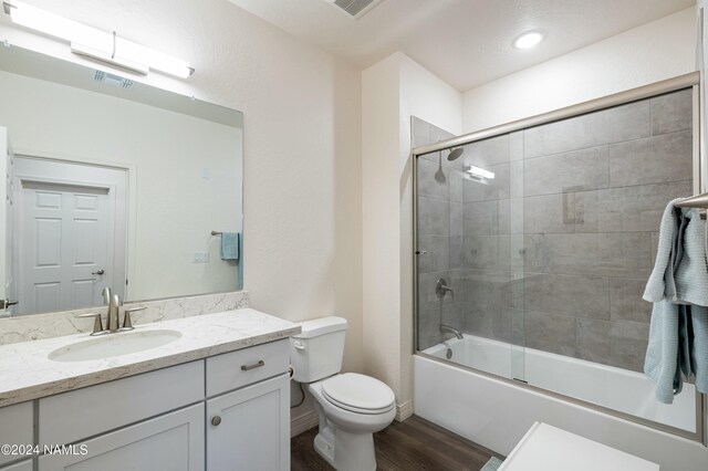 full bathroom with vanity, hardwood / wood-style floors, shower / bath combination with glass door, and toilet