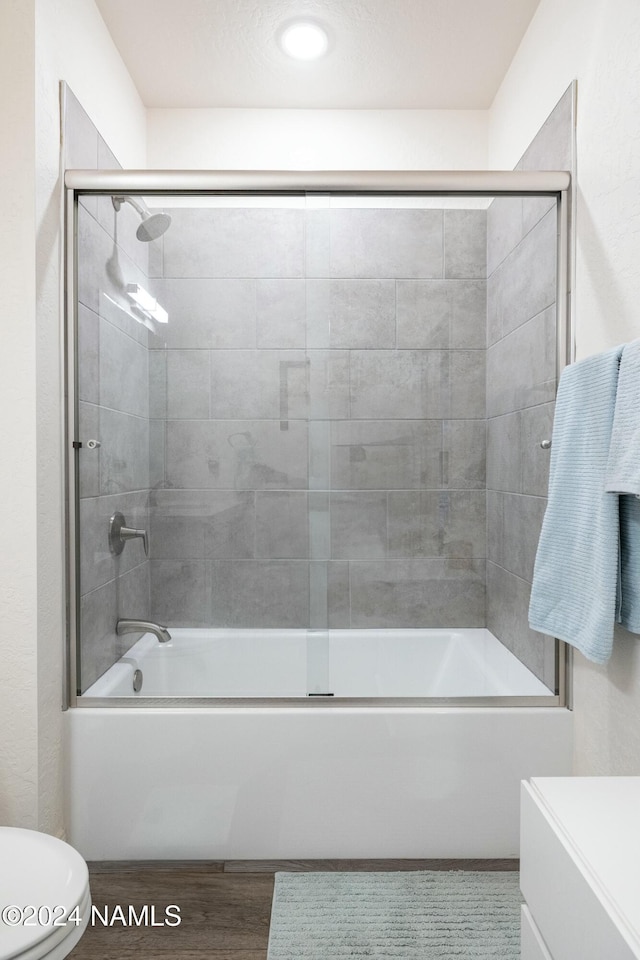 bathroom with wood-type flooring, toilet, and combined bath / shower with glass door