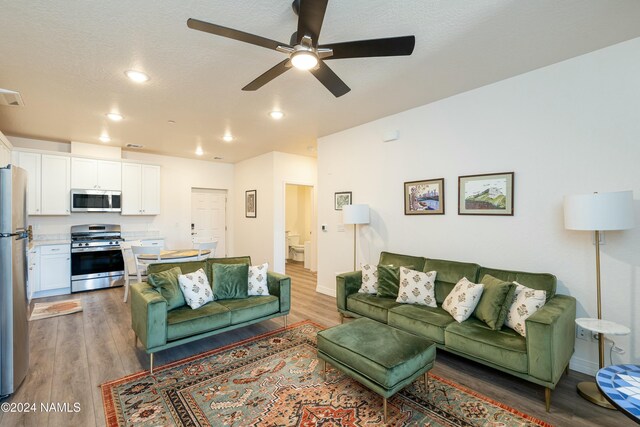 living room featuring wood-type flooring, a textured ceiling, and ceiling fan