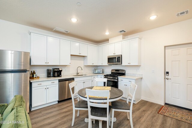 kitchen featuring hardwood / wood-style flooring, stainless steel appliances, sink, and white cabinets