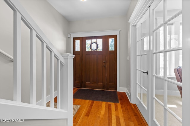 foyer entrance with stairway, wood finished floors, and baseboards