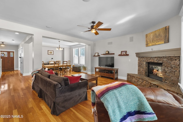 living area with baseboards, a stone fireplace, wood finished floors, and a ceiling fan