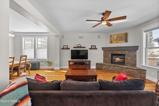 living room with a stone fireplace, wood finished floors, baseboards, and a wealth of natural light