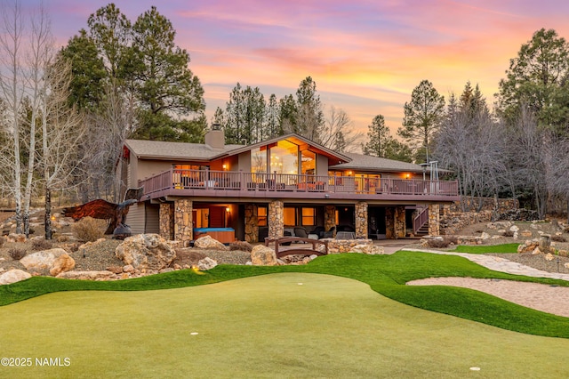 back house at dusk featuring a wooden deck and a patio