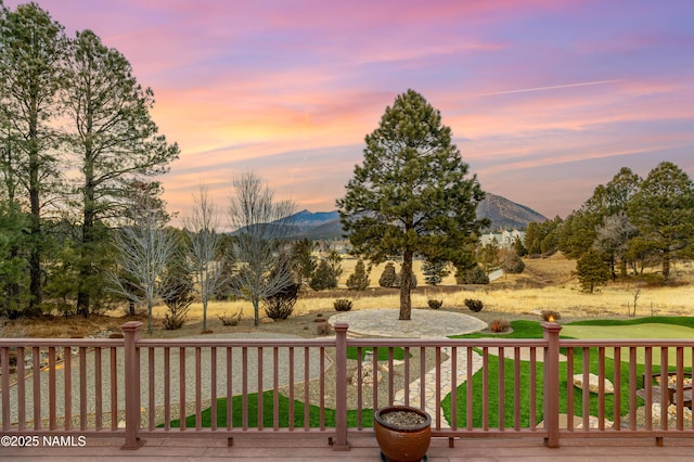 deck at dusk featuring a yard and a mountain view