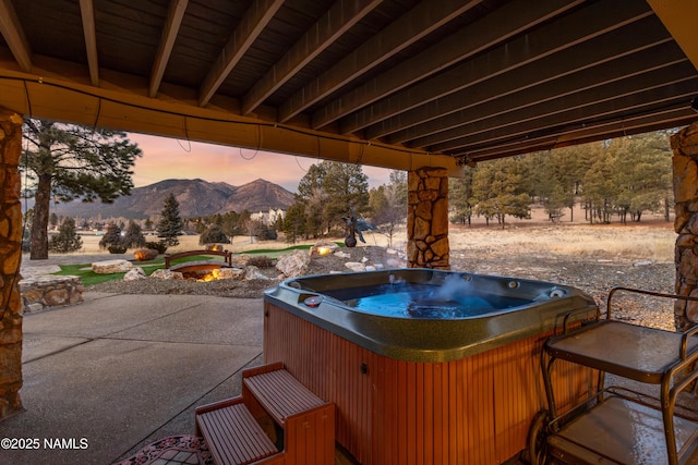 patio terrace at dusk featuring a hot tub and a mountain view