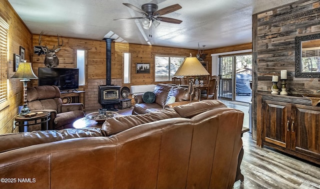 living room with a textured ceiling, wooden walls, a ceiling fan, and wood finished floors